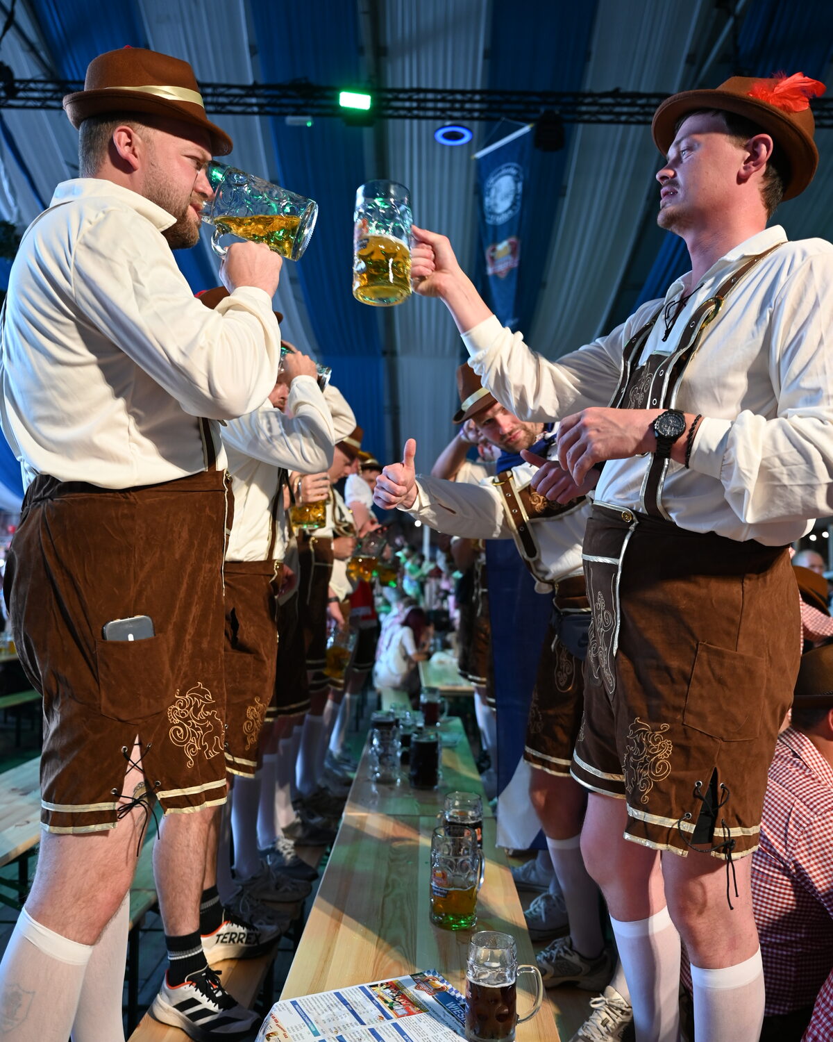 Zwei Gäste in Lederhosen stoßen im Festzelt mit Maßkrügen an